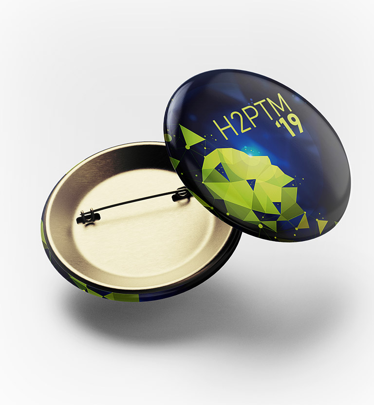 Badge à épingle métallique reprenant le visuel abstrait de l'affiche et le titrage simplifié «&nbsp;H2PTM'19&nbsp;».